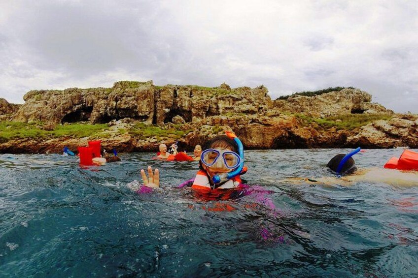 Une personne portant un gilet de sauvetage rouge et du matériel de plongée en apnée, dans l'eau, avec des falaises rocheuses en arrière-plan. 5
