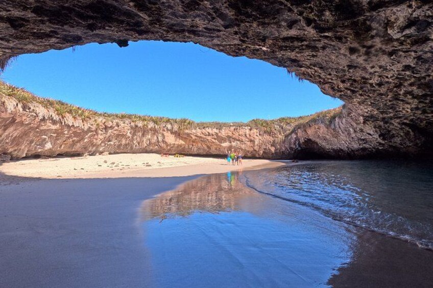 Une plage avec une entrée de grotte, un ciel bleu dégagé et une eau calme. 1
