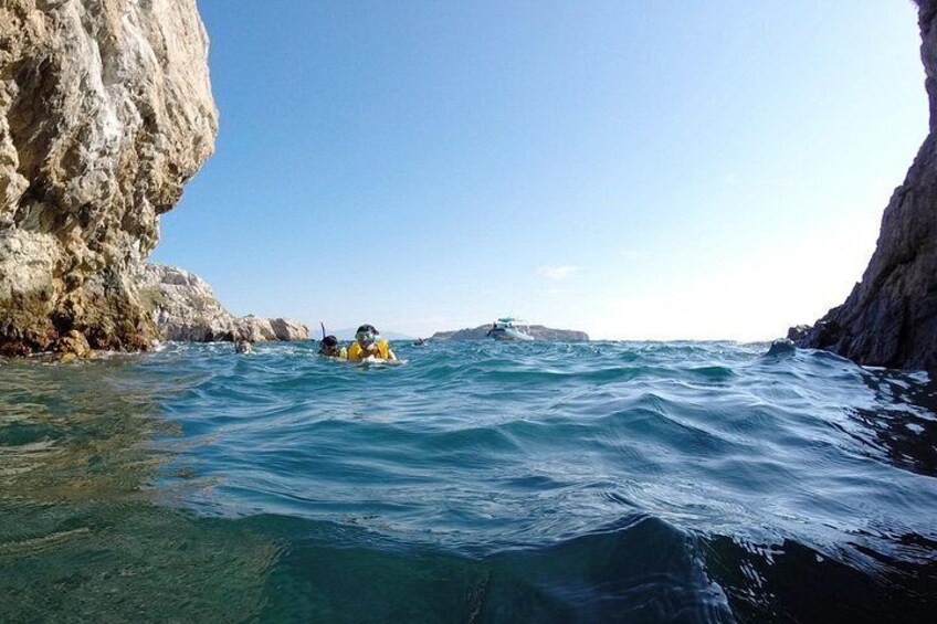 A rocky coastline with clear blue water, a person in a kayak, and a distant boat. 5