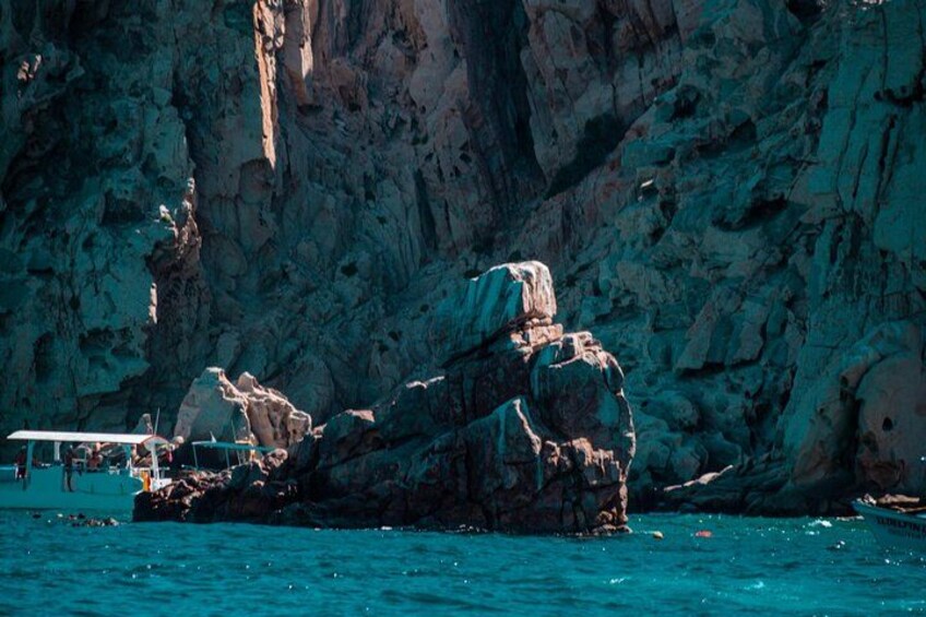 Un afloramiento rocoso en el agua con un barco al fondo. 4