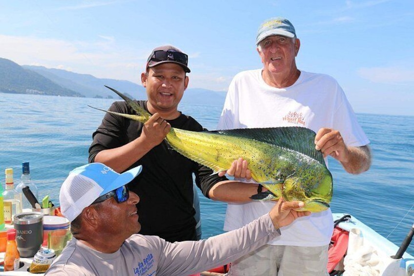 Tre persone che mostrano un grande pesce su una barca, con un lago e montagne sullo sfondo. 1