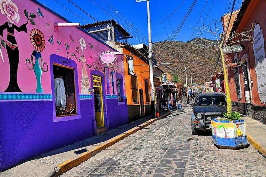 A cobblestone street with colorful buildings, a parked car, and a mountain in the background. 4