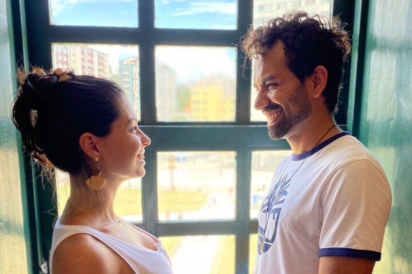 Two people standing in front of a window with a view of buildings. 2