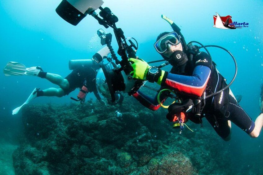 Two scuba divers underwater with cameras, surrounded by marine life and coral formations. 4