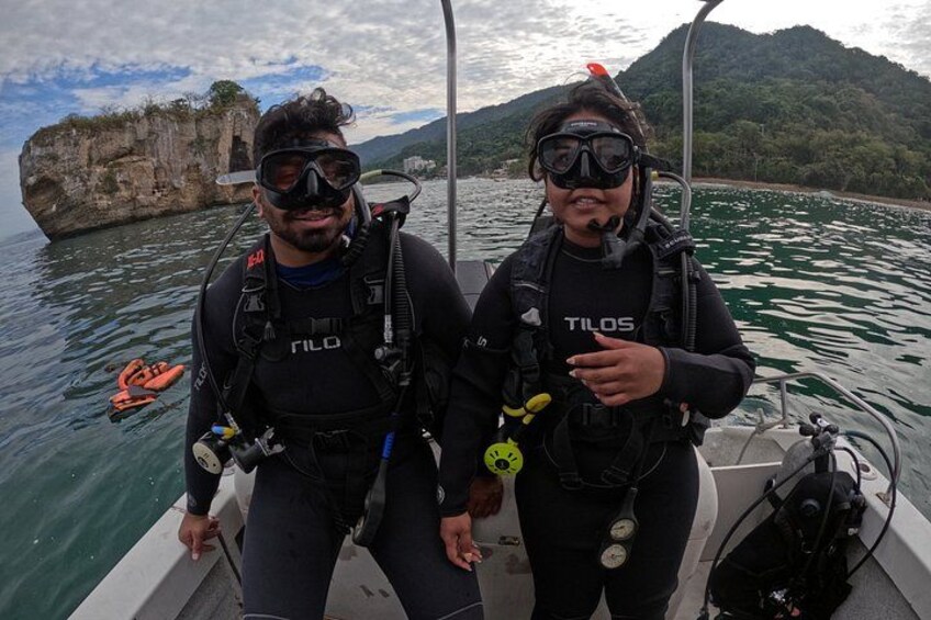 Two scuba divers on a boat with a rocky coastline in the background. 2