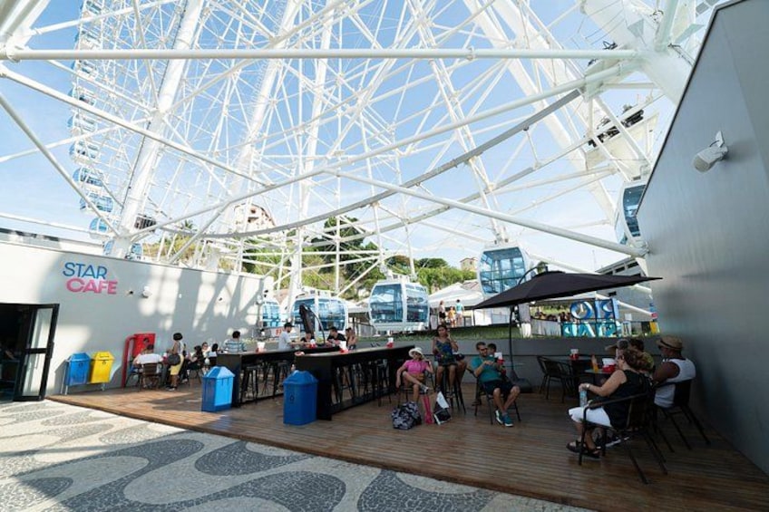 A cruise ship deck with a Ferris wheel, a bar area, and people sitting and standing. 2