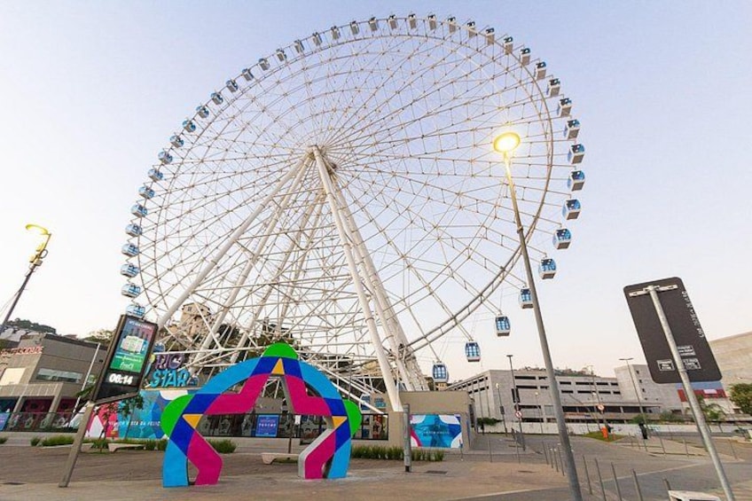 A large Ferris wheel, a colorful archway, and a street with shops and signs. 4