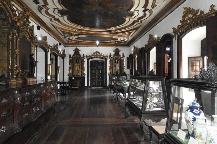 An ornate room with dark wooden floors, elaborate wall decorations, and a large mirror. 2