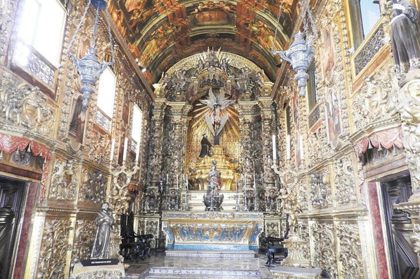 Een versierd kerkinterieur met gedetailleerde houtsnijwerken, een centraal altaar en een standbeeld. 2