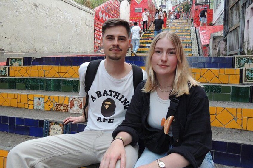 Twee personen zitten op kleurrijke betegelde treden, met een trap op de achtergrond. 3