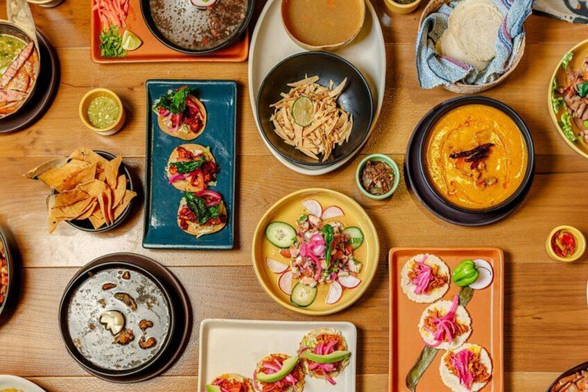 Une variété de plats sont disposés sur une table en bois, notamment des tacos, un bol de soupe et une assiette de légumes coupés en tranches. 4
