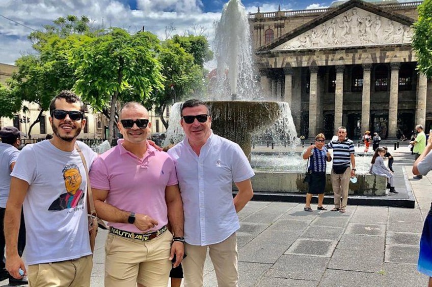 Tres personas frente a una fuente, con un edificio clásico al fondo. 5
