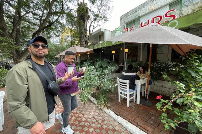 Dos hombres de pie frente a un restaurante con terraza, un espacio al aire libre con plantas y un camino de ladrillo. 4
