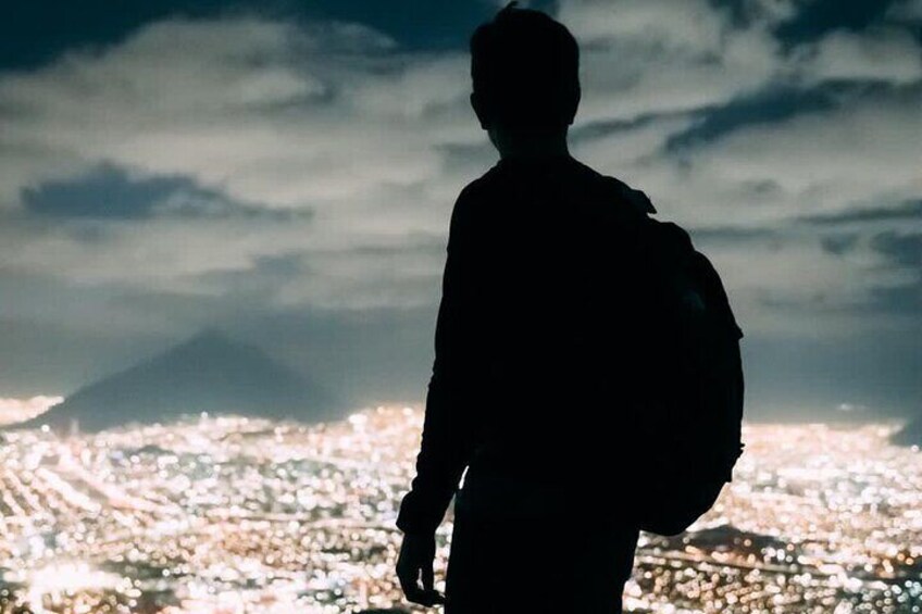 A silhouette of a person with a backpack against a cityscape and a mountain in the background. 3