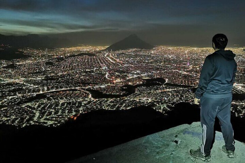 A person standing on a cliff overlooking a city at night. 2