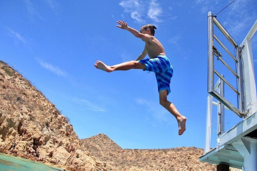 Una persona saltando desde una plataforma de clavados hacia un cuerpo de agua con acantilados rocosos al fondo. 4
