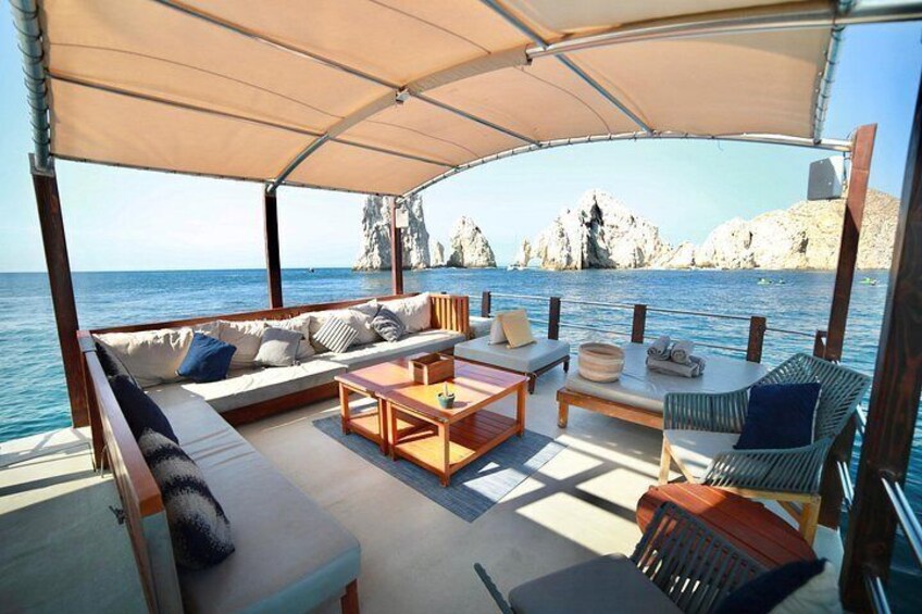 A covered outdoor seating area on a boat with a view of rocky cliffs and the sea. 2