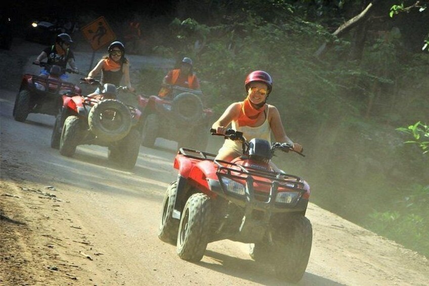 People riding ATVs on a dirt road surrounded by greenery. 1