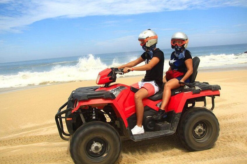 Two people on a red ATV on a sandy beach with waves in the background. 3