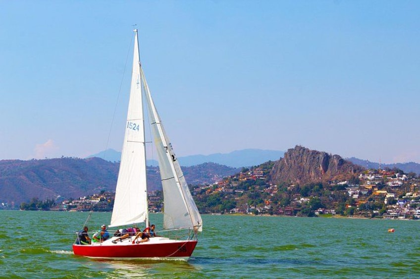 A sailboat with a white sail on a body of water, with a mountainous landscape in the background. 1