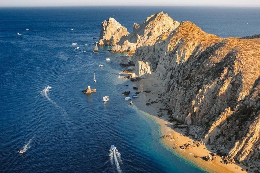 A coastal landscape with rocky cliffs, a sandy beach, and boats in the water. 1