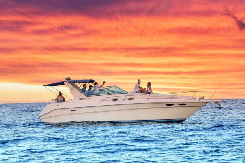 A white boat with people on it, sailing on the water during sunset. 1
