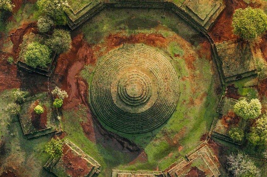 An aerial view of a circular stone structure surrounded by greenery and trees. 1