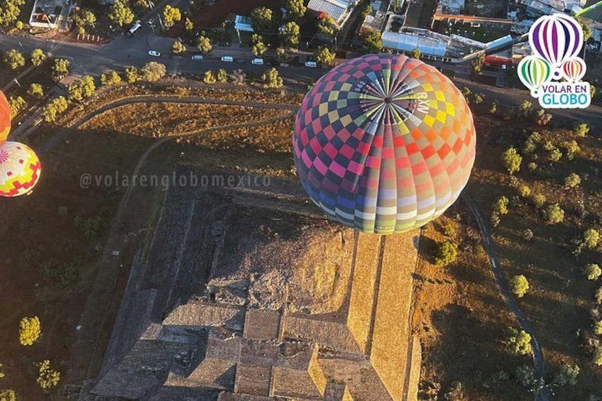 Un globo aerostático con un diseño colorido sobrevuela un paisaje con edificios y árboles. 1