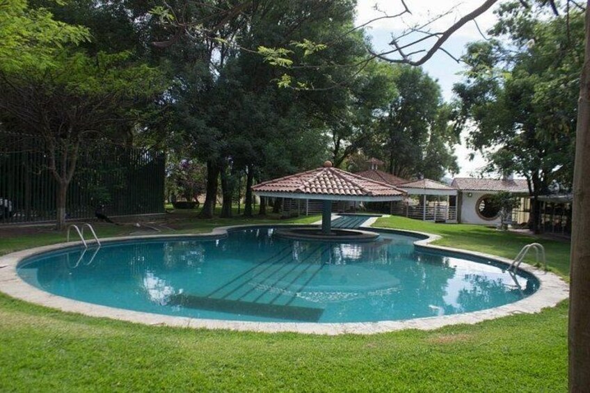 A swimming pool with a tiled deck, surrounded by grass and trees. 2