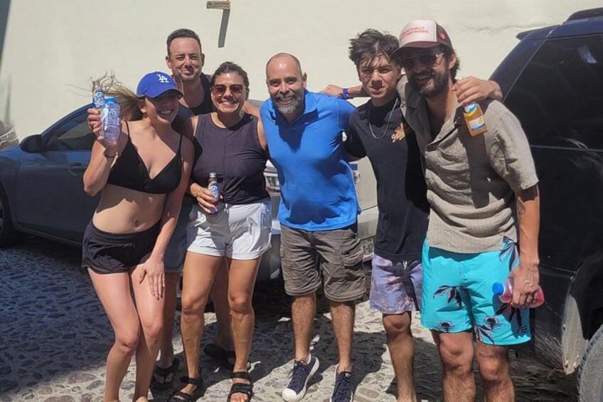 Un gruppo di persone in piedi all'aperto, alcune con bevande in mano, con un'auto e un edificio sullo sfondo. 4