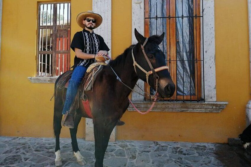 Une personne à cheval devant un bâtiment jaune avec une fenêtre grillagée. 4