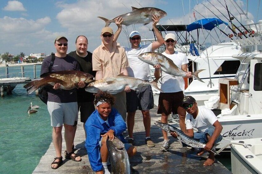 A group of people on a dock holding fish, with a boat and water in the background. 3