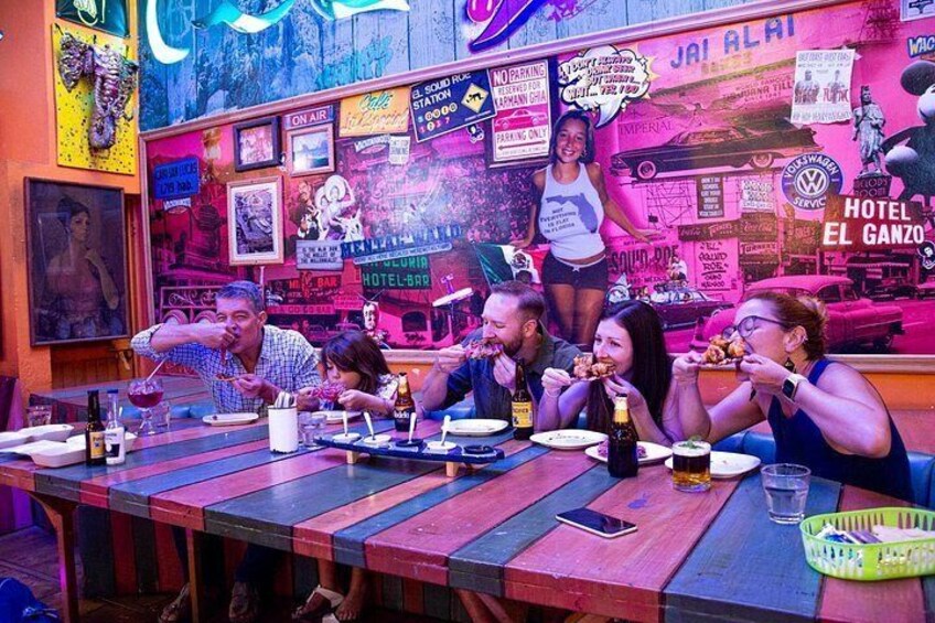 En gruppe mennesker spiser på en farverig restaurant med neonlys og plakater på væggene. 2
