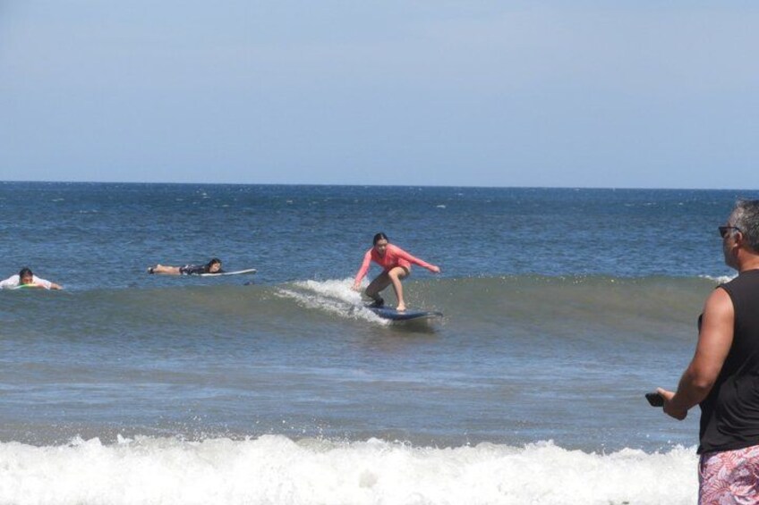 A surfer riding a wave, other surfers in the water, and a beachgoer watching. 4