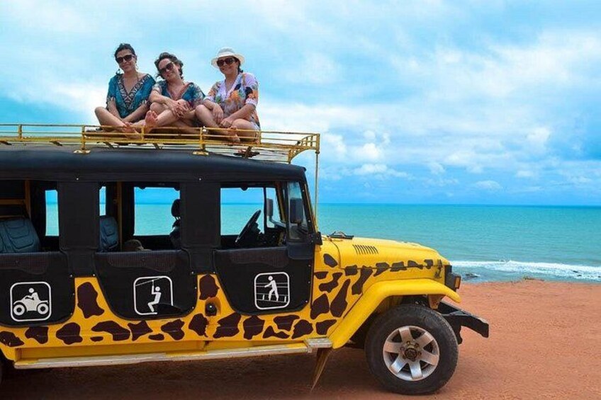 A safari vehicle with three passengers on a beach. 5