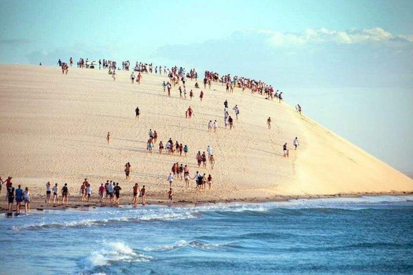 A crowded beach with people walking up a sandy slope towards the water. 1