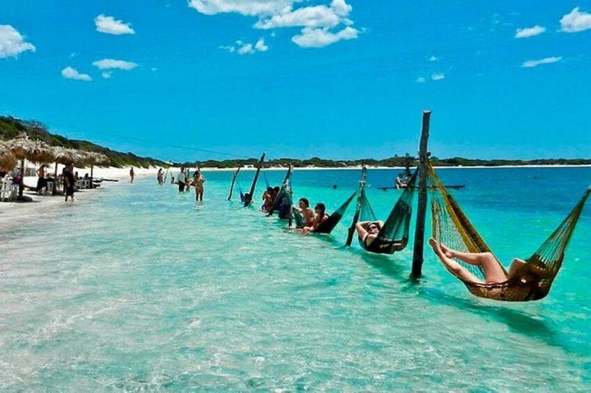 A beach with clear turquoise water, people relaxing in hammocks, and thatched-roof structures in the background. 3