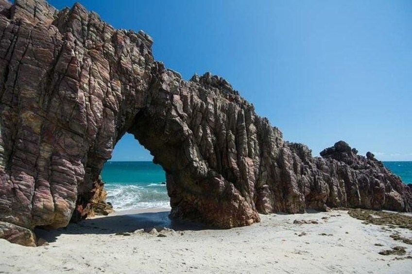 Formación rocosa en arco sobre una playa, con agua azul cristalina al fondo. 5