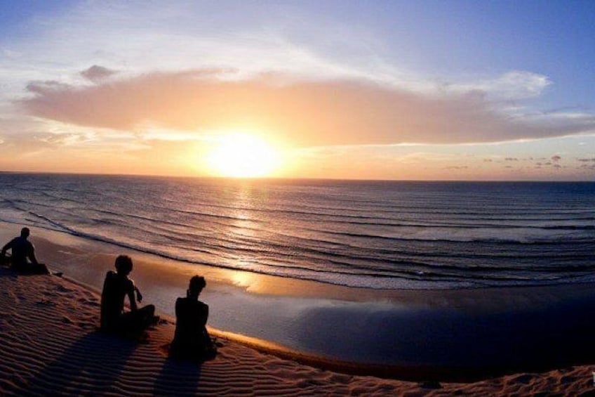 Solnedgang over havet med folk siddende på stranden. 2