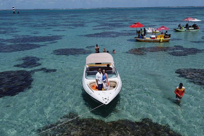 A boat anchored near clear blue waters with rocky seabed, surrounded by other boats and people. 2