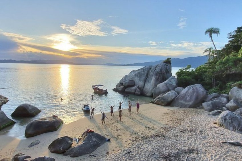 A beach with large rocks, a boat, and people enjoying the sunset. 1