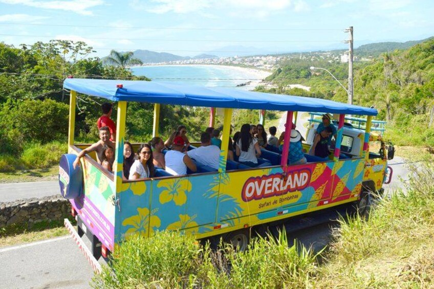 A colorful overland safari vehicle with passengers, surrounded by lush greenery and a coastal view. 3