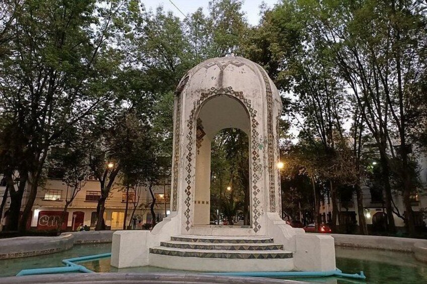 A white arched structure with decorative patterns, surrounded by trees and a water feature. 2