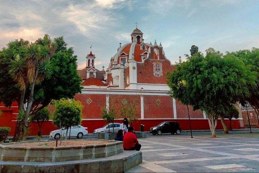 A historic building with a red facade and white accents, surrounded by trees and a paved plaza with cars. 4