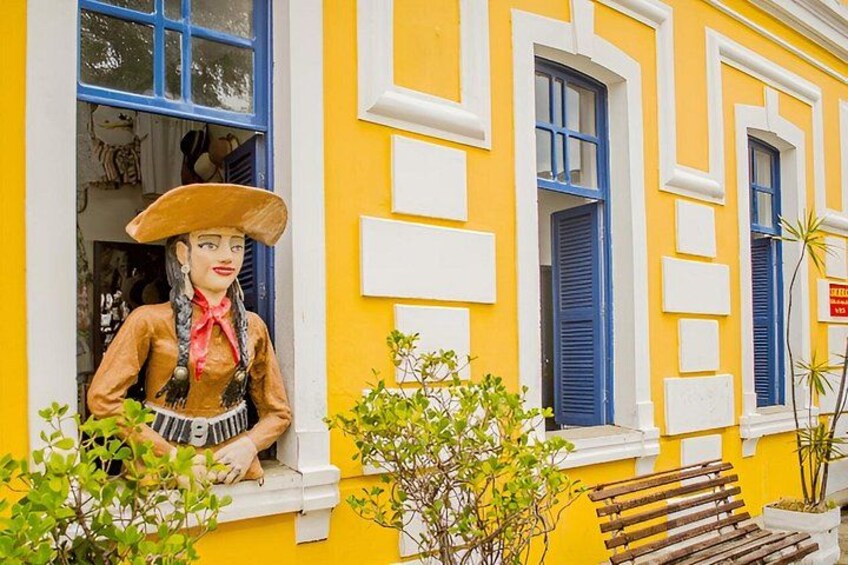 A yellow building with blue shutters, a wooden bench, and a statue of a woman in a hat. 3