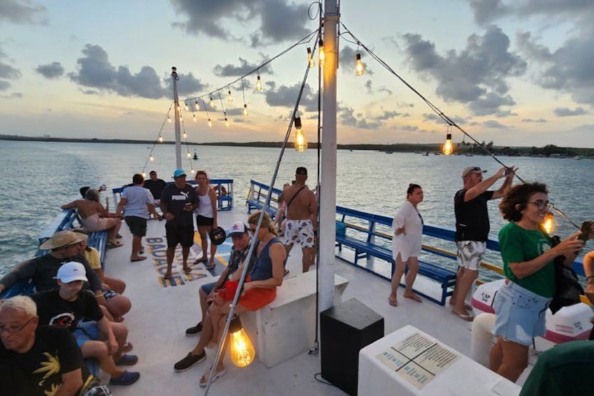A boat with people on deck, string lights, and a sunset in the background. 5