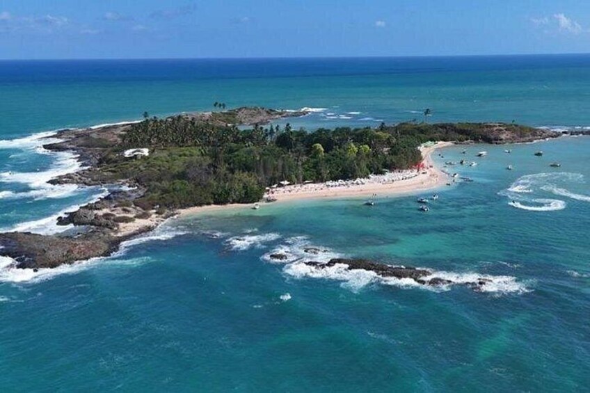An aerial view of a tropical island with a beach, clear turquoise waters, and scattered boats. 1