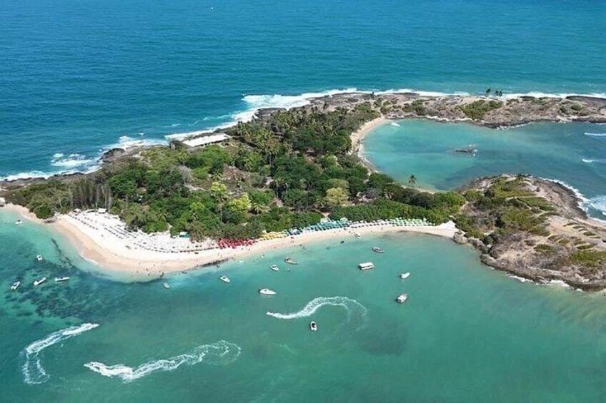 An aerial view of a tropical island with a beach, clear turquoise waters, and scattered boats. 3
