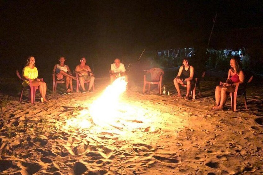 A group of people sitting around a campfire on a sandy beach at night. 4