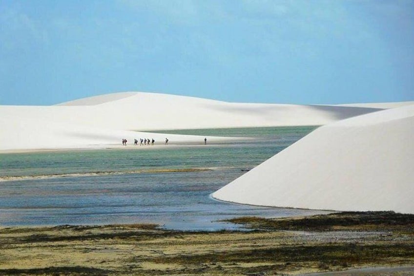Sand dunes, a body of water, and a group of people walking. 5